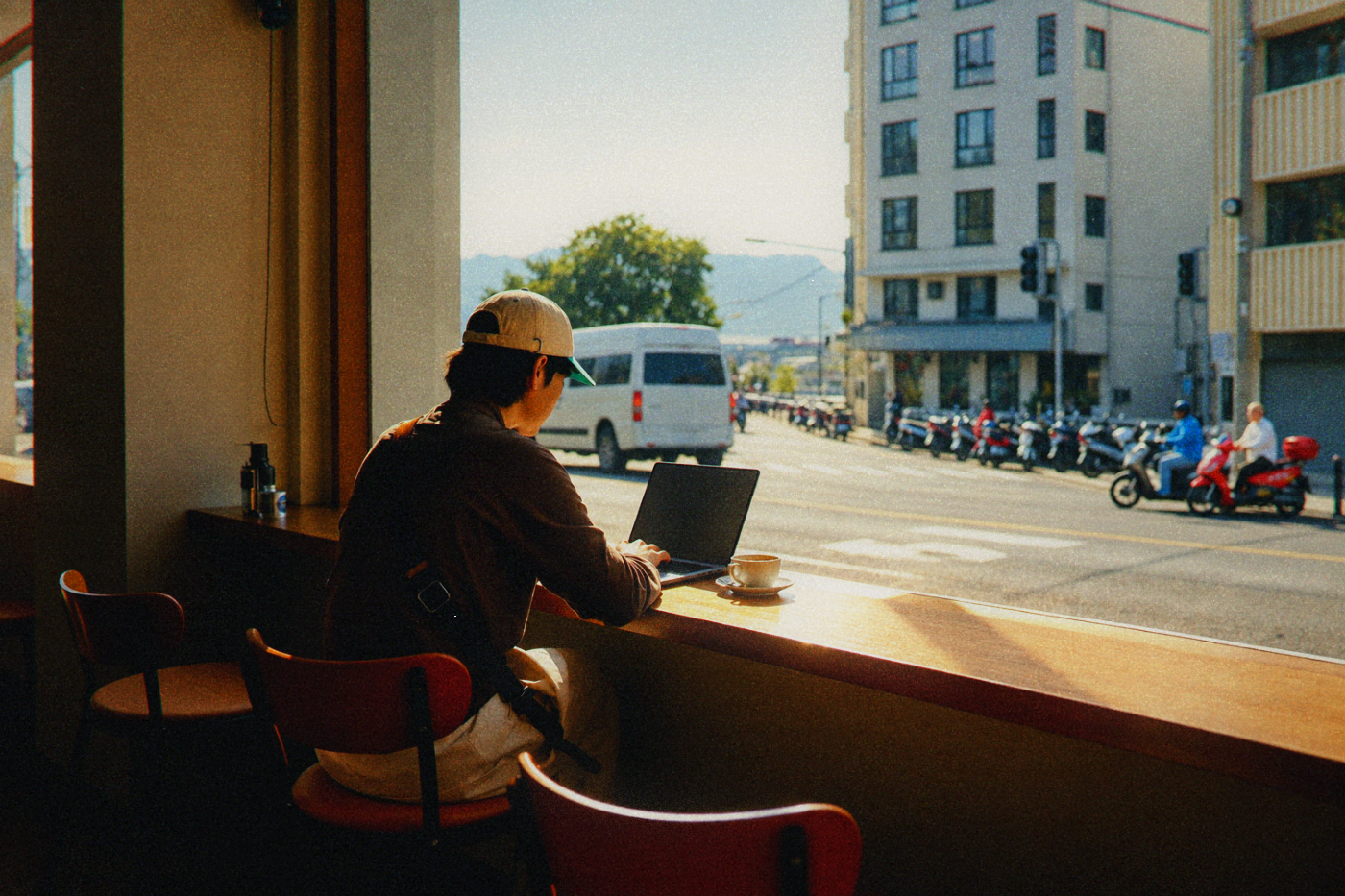 Person wearing a cap working beside a cafe window overlooking a street