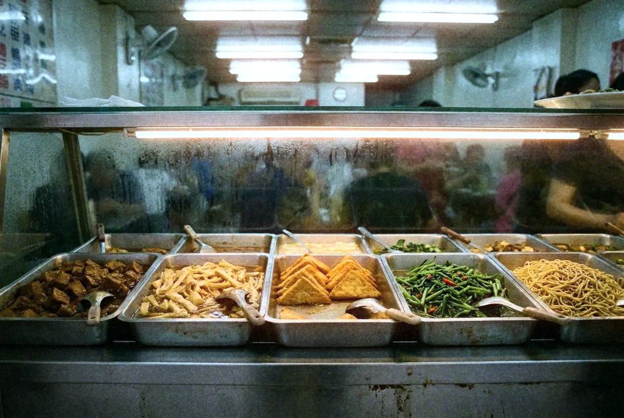 A bustling vegetarian buffet counter with dozens of colorful dishes in metal trays