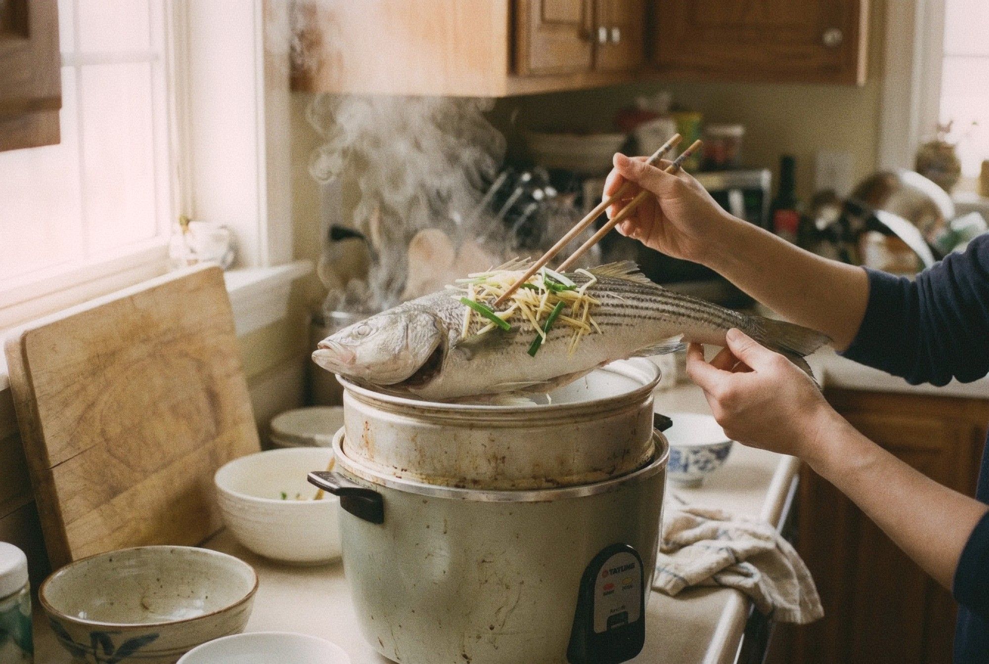 Whole steamed fish with ginger and scallions being lifted from inside a Tatung rice cooker inner pot