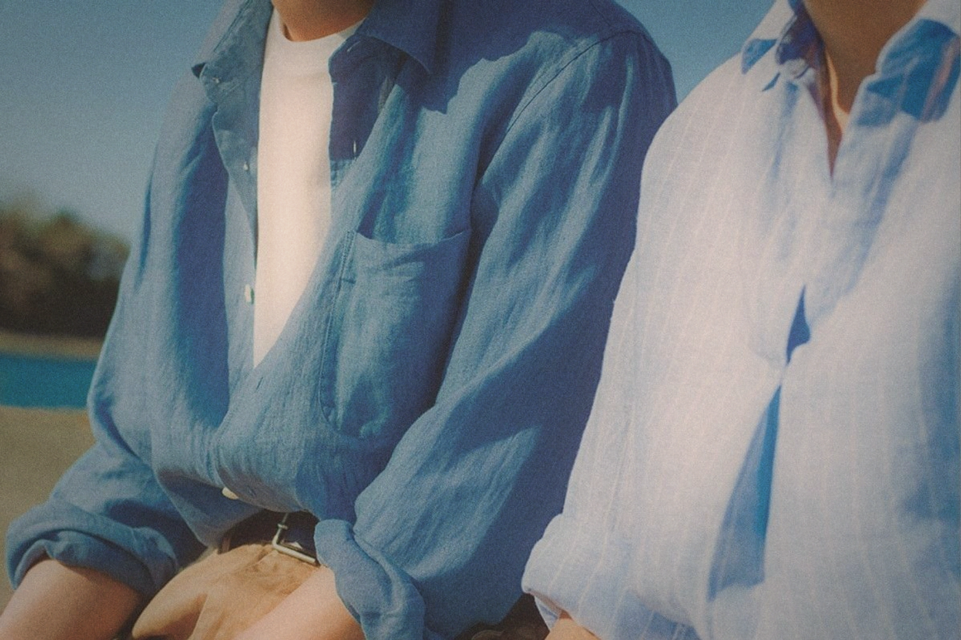 Two people in loose linen shirts, one blue and one white-striped, cropped at the shoulders in bright sun