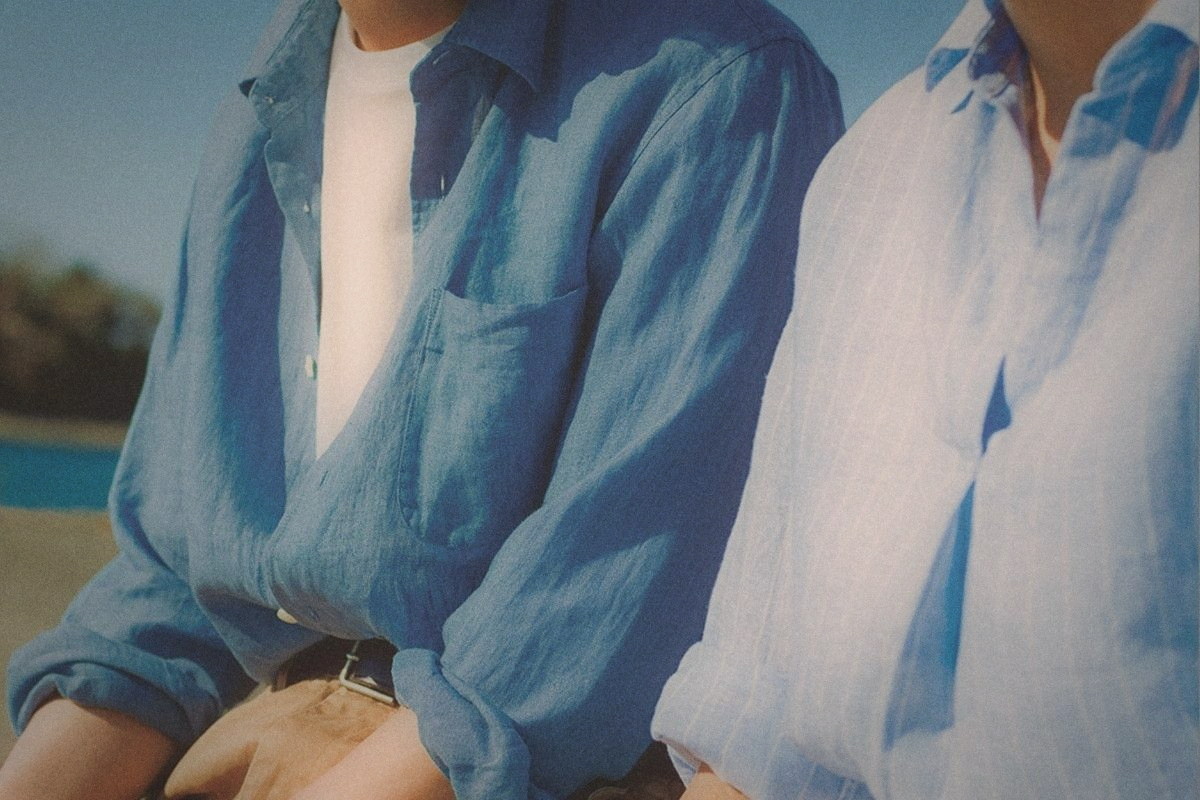 Two people in loose linen shirts, one blue and one white-striped, cropped at the shoulders in bright sun