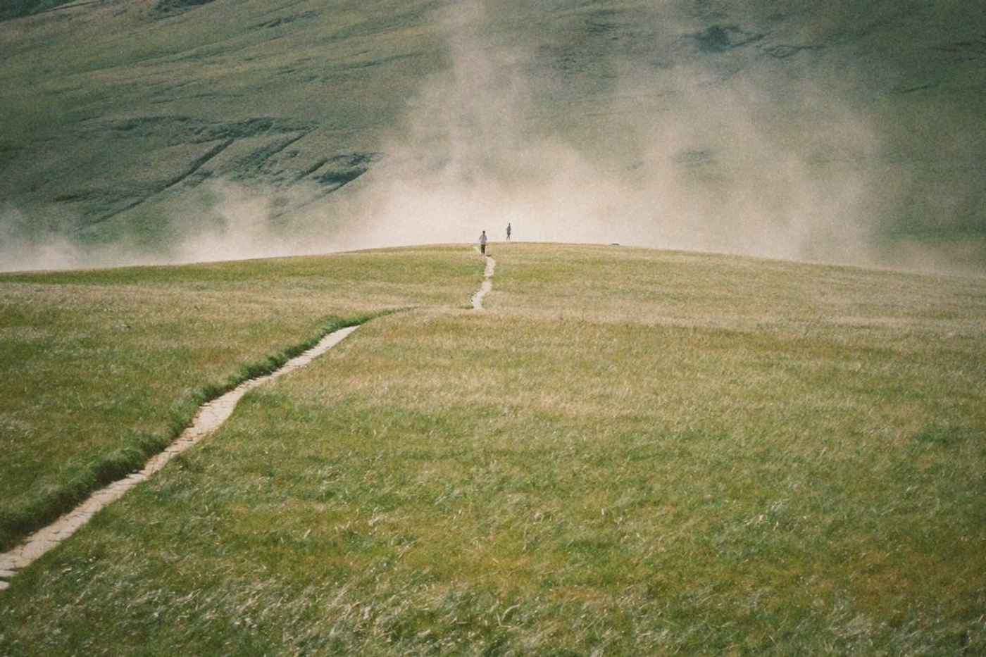 Open windswept grassland plateau on a mountain above Taipei with mist drifting over the grass and hikers on a stone path
