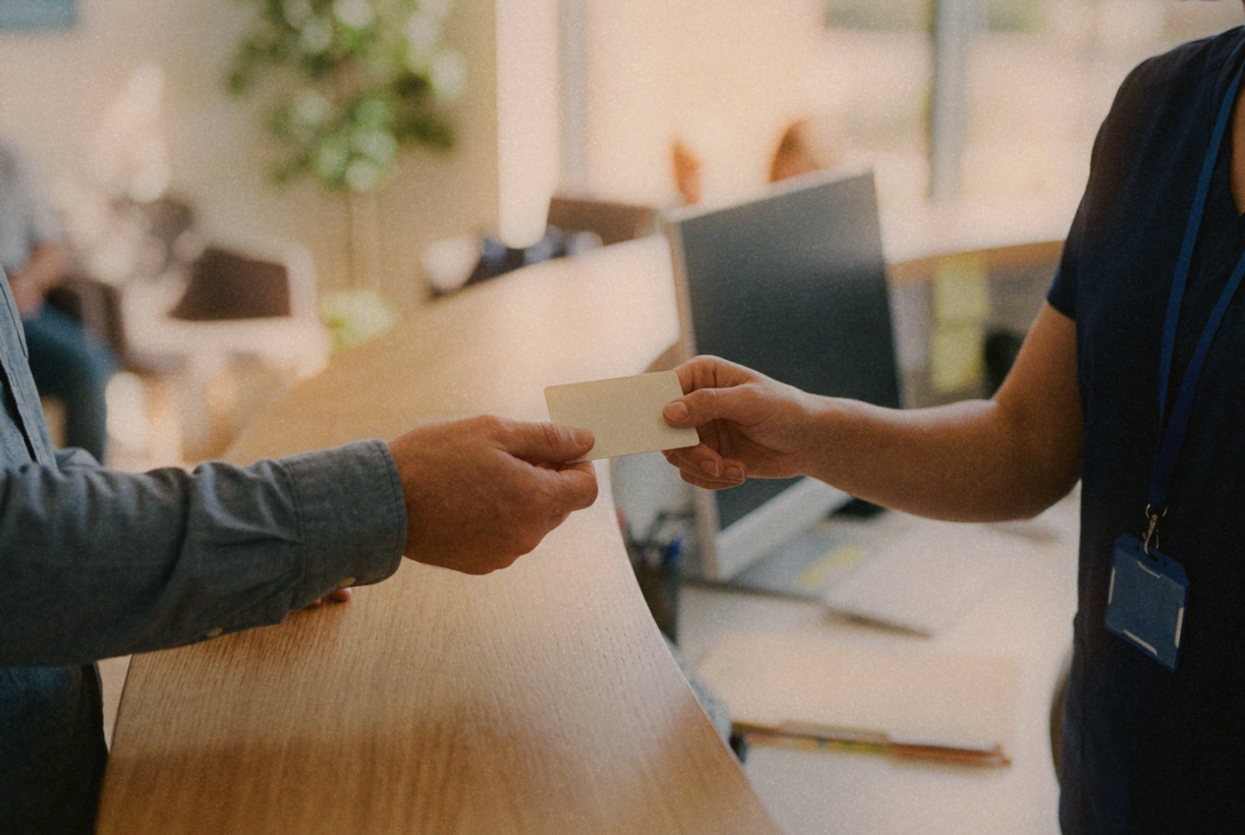 Two hands passing a plain health card across a clinic reception counter