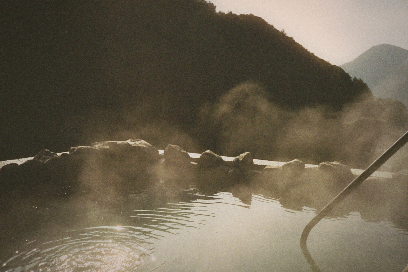 Natural rock hot spring pool surrounded by misty steam and rugged stone formations