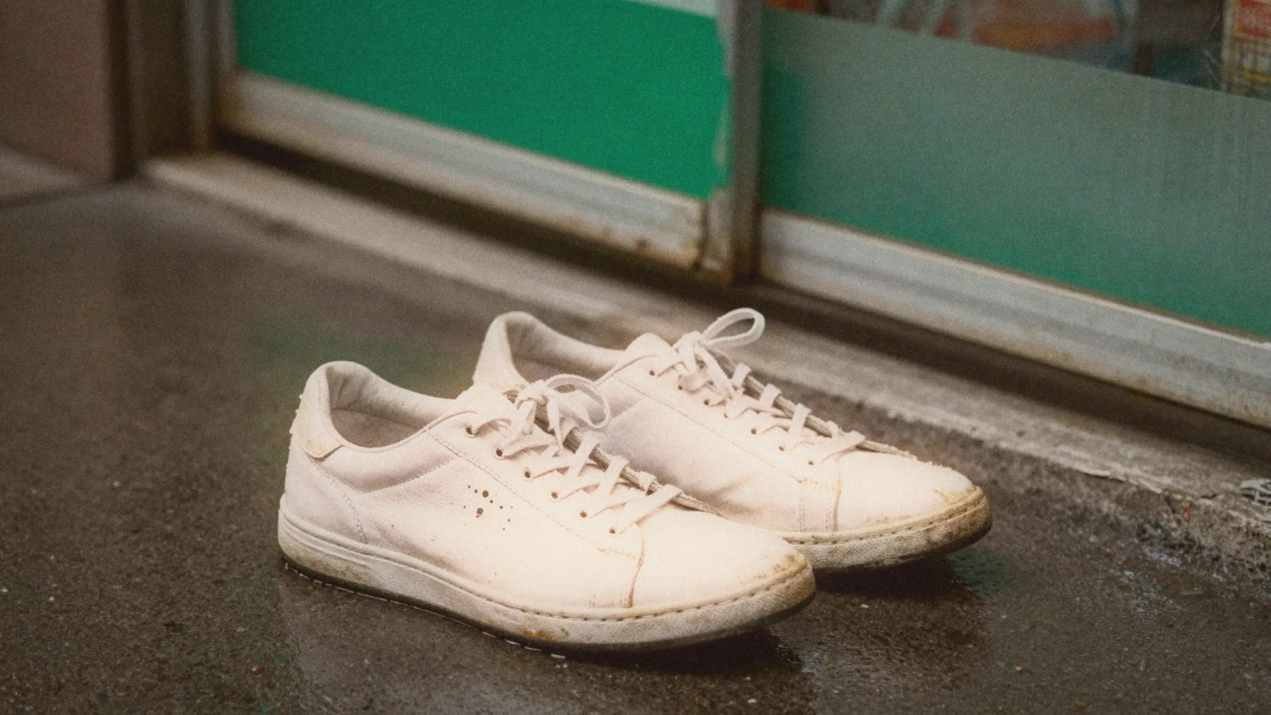 A pair of ruined wet white sneakers on a rainy Taipei sidewalk near a FamilyMart awning