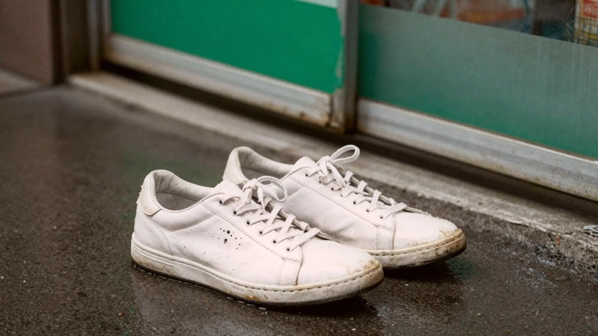 A pair of ruined wet white sneakers on a rainy Taipei sidewalk near a FamilyMart awning