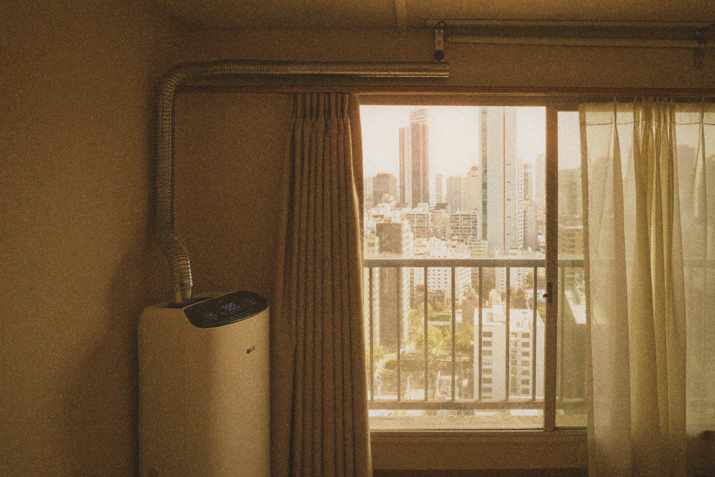 Portable air purifier standing beside a window with Taipei city skyline visible through sheer curtains