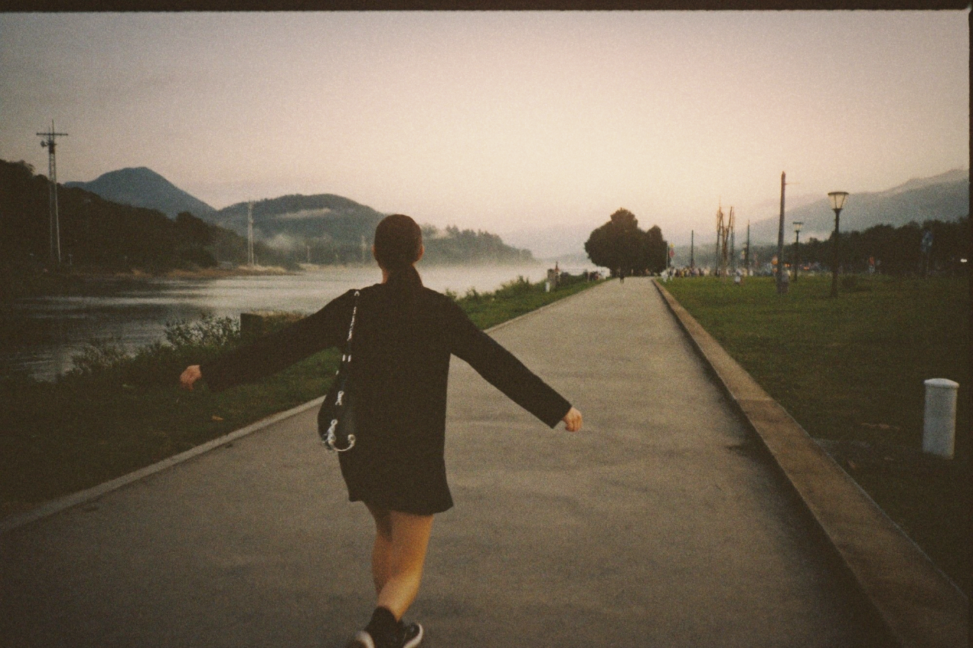 Woman walking mindfully along a misty riverside path at dawn with arms gently spread