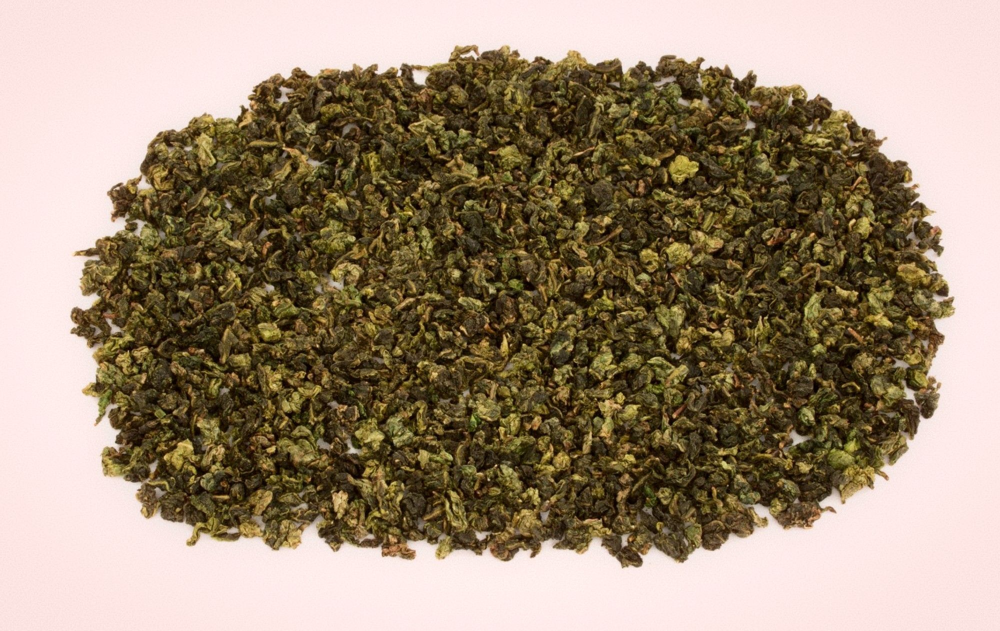 Loose rolled oolong tea leaves spread in an oval on a pale pink surface