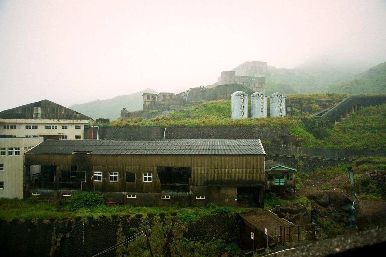 Derelict mine buildings and concrete silos on a misty green hillside