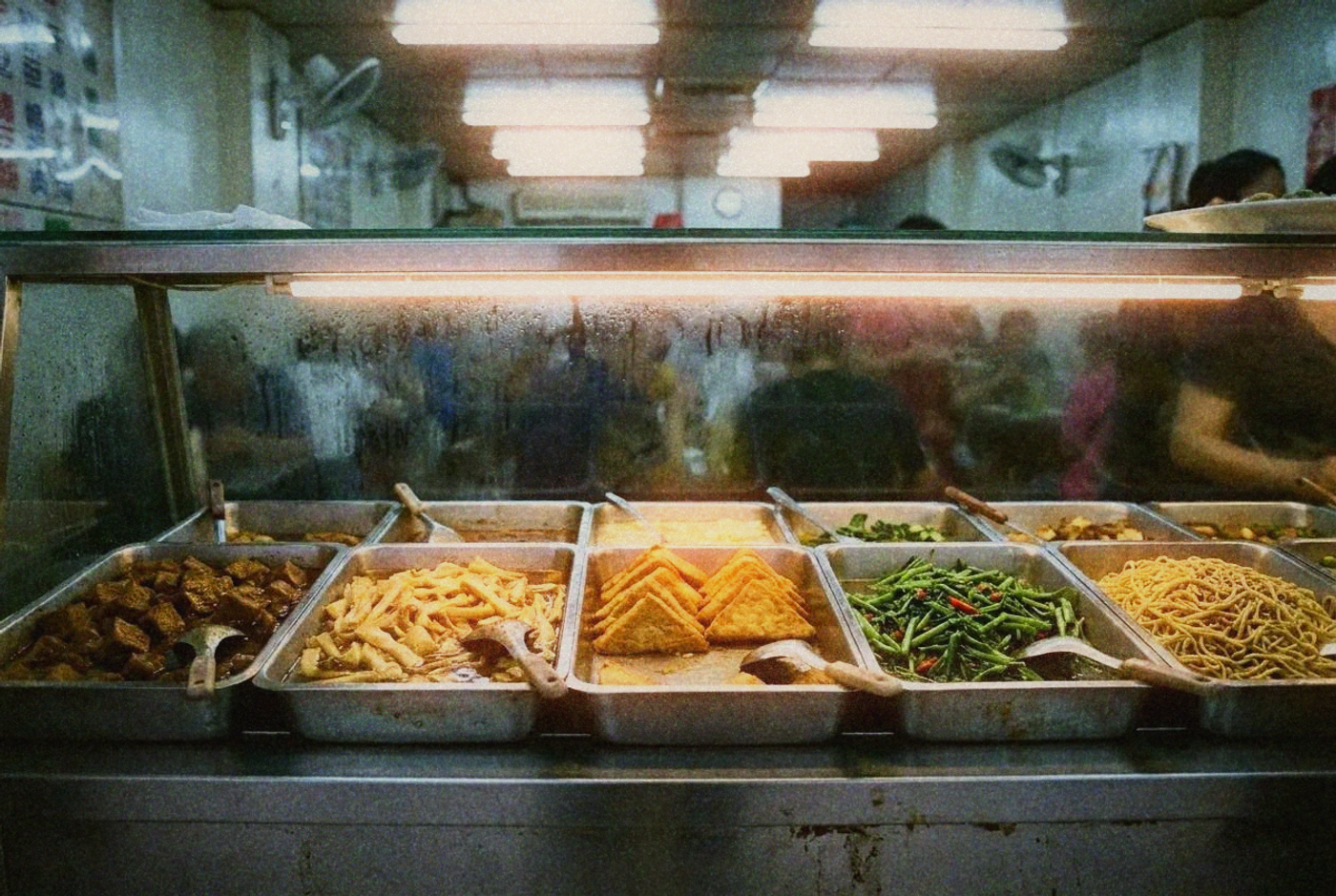 A bustling vegetarian buffet counter with dozens of colorful dishes in metal trays