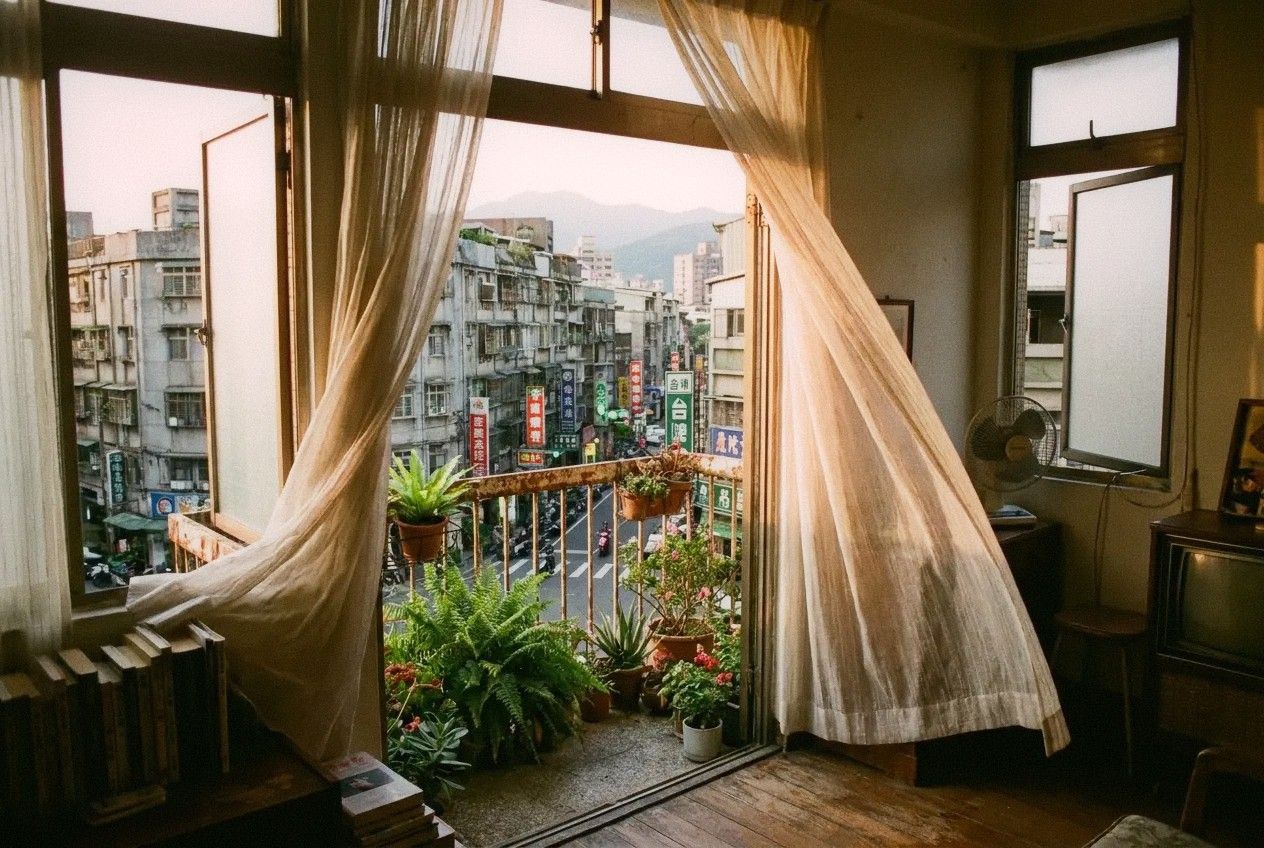 View from inside a Taipei apartment looking out through an open window with sheer curtains catching a breeze