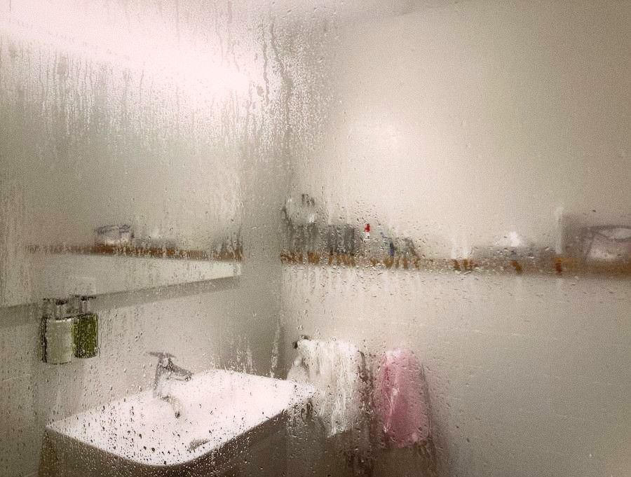 A small Taipei apartment bathroom with condensation on the mirror and toiletries crowded on limited surfaces