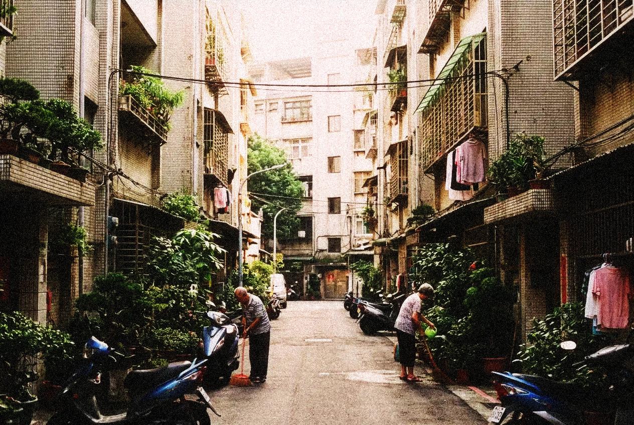 A quiet residential alley in a Taipei neighborhood with potted plants and warm morning light