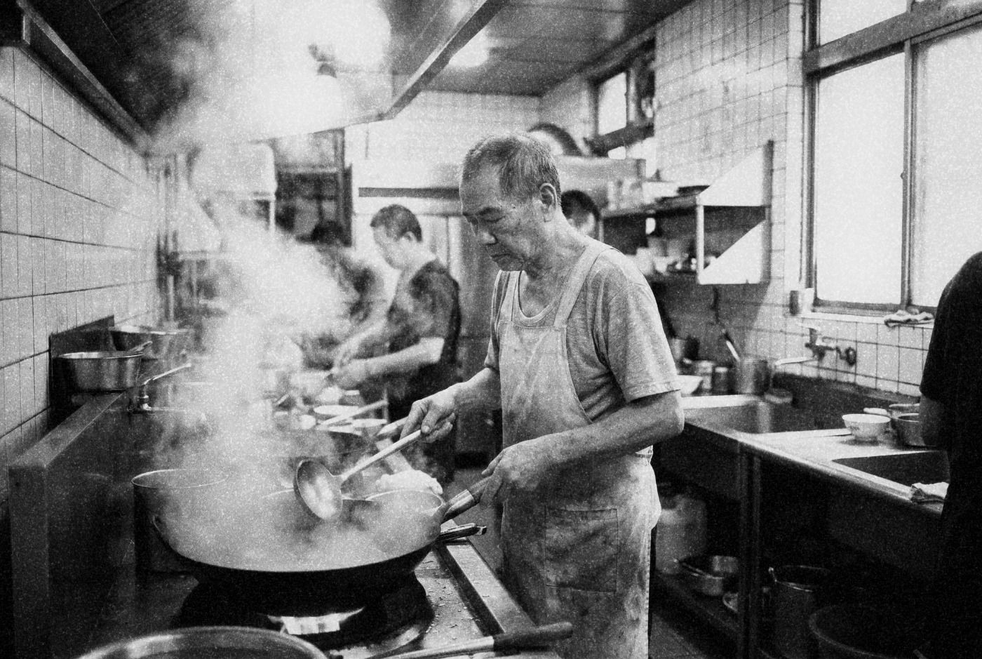 Elderly Taiwanese cook at a wok station in a traditional restaurant kitchen