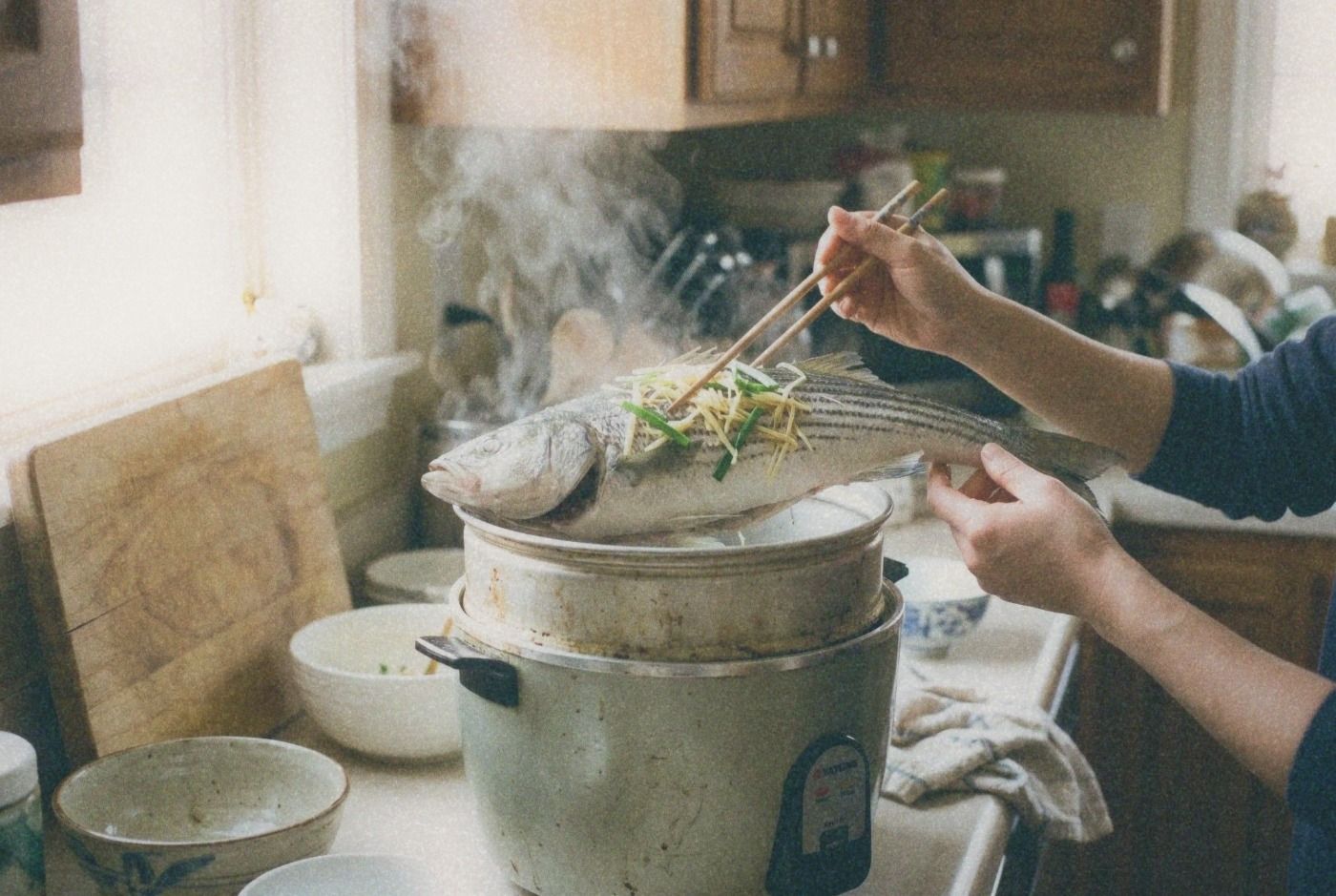 Whole steamed fish with ginger and scallions being lifted from inside a Tatung rice cooker inner pot