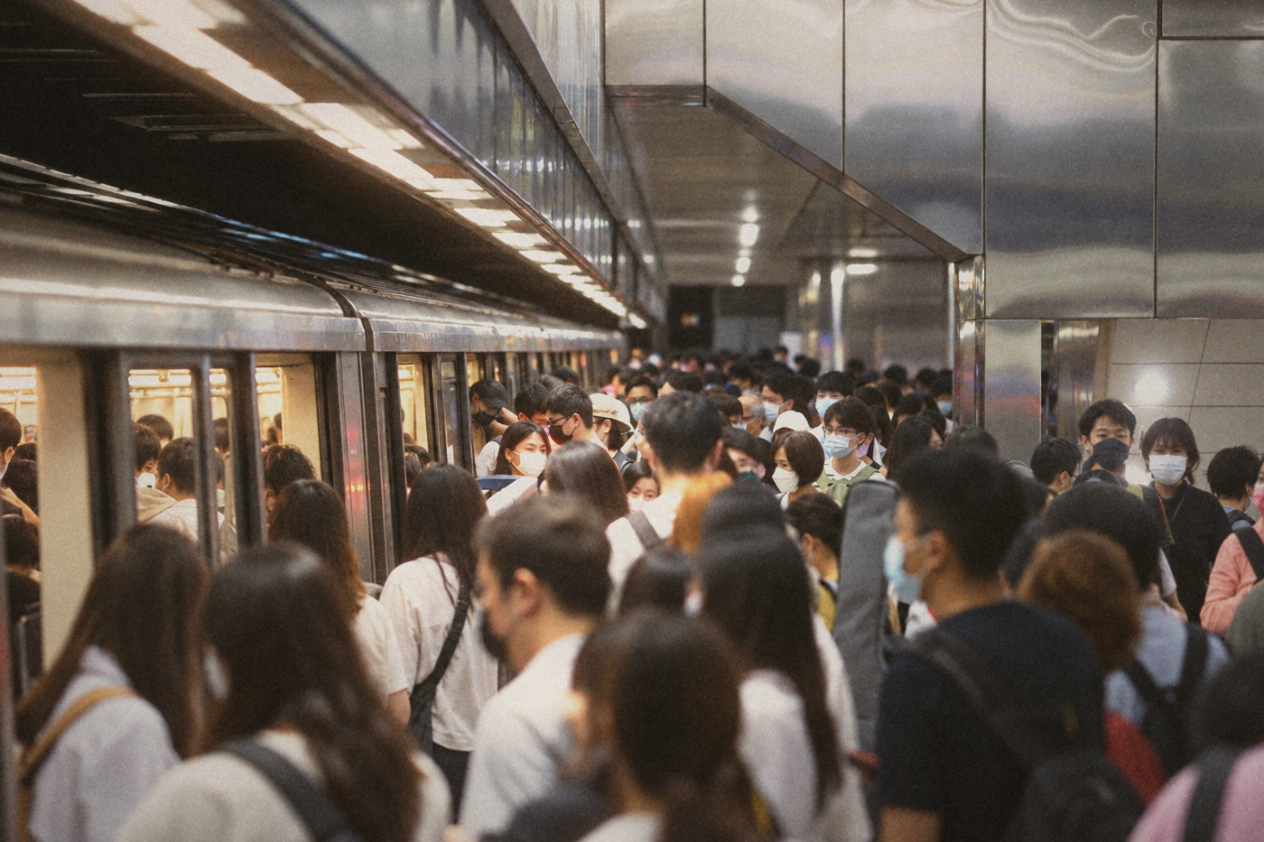 Crowded subway platform packed with masked commuters boarding a train