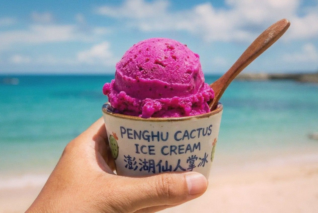 Bright pink-purple scoop of prickly pear cactus ice cream held against ocean background