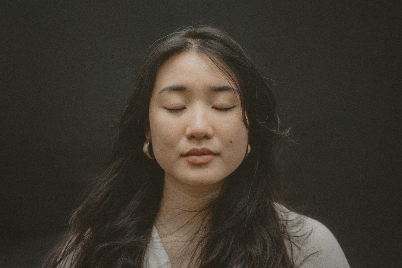 Close portrait of a woman with long dark hair and her eyes closed against a dark background