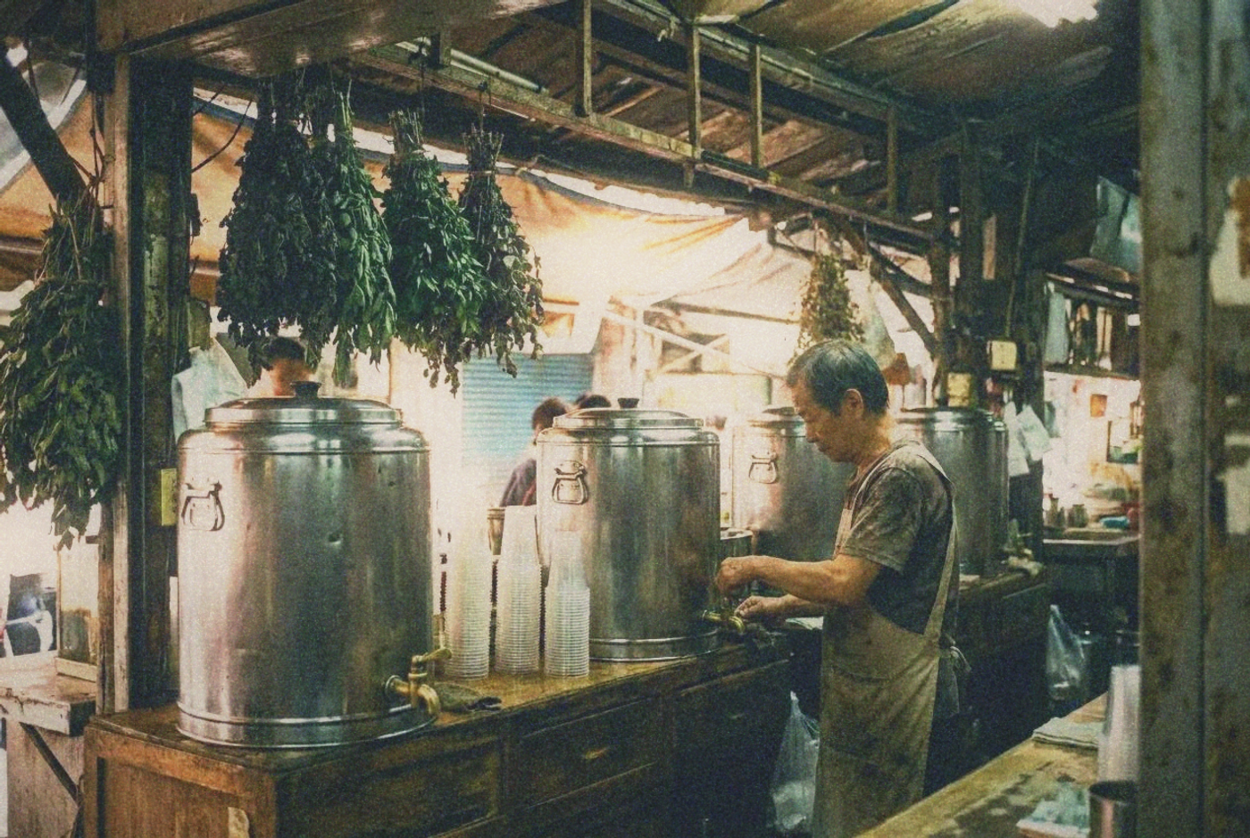 A herbal tea stall with large steel urns and stacks of plastic cups at a Taipei market