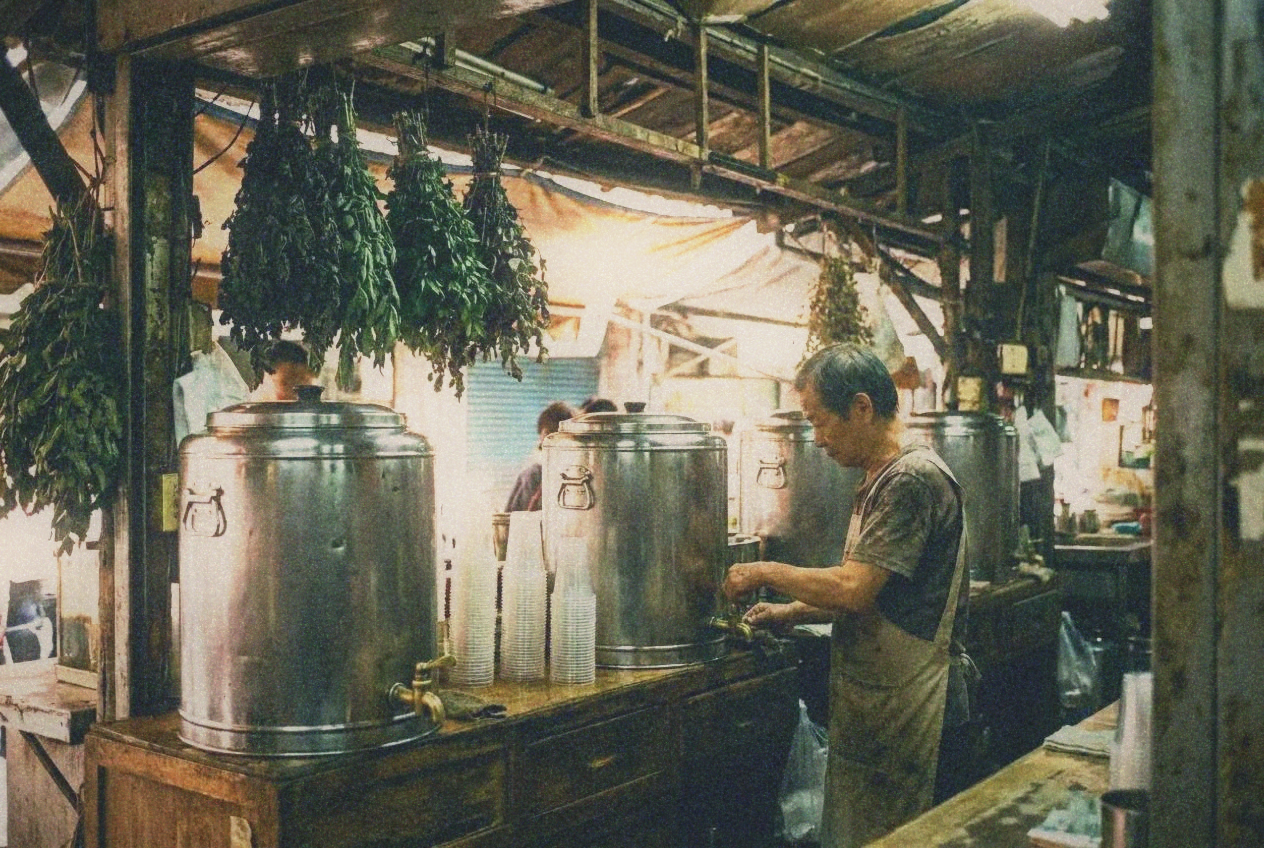 A herbal tea stall with large steel urns and stacks of plastic cups at a Taipei market
