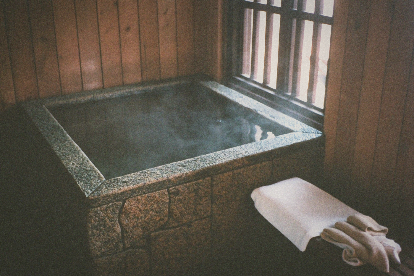 Private indoor hot spring bath with steam rising from a stone tub by a window