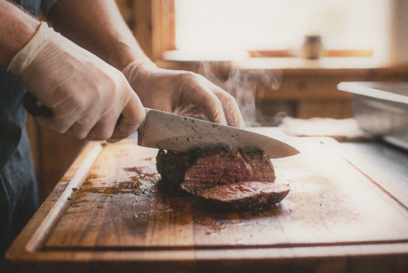 Close-up of butcher hands slicing fresh warm beef on a worn wooden cutting board