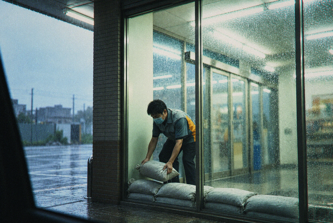 A worker stacks sandbags inside a rain-soaked storefront.