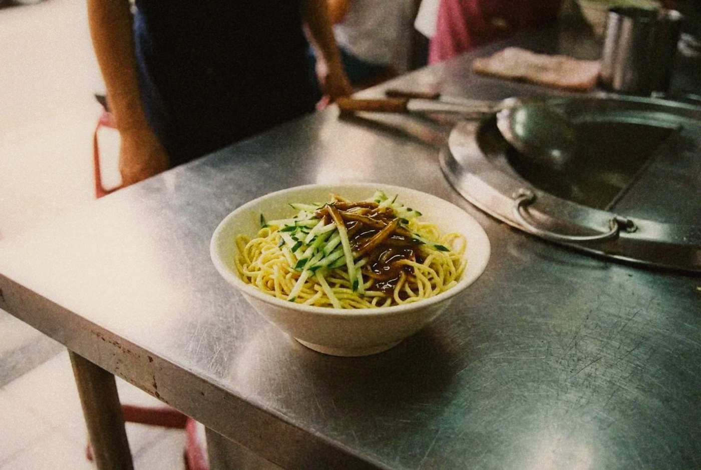 A bowl of Taiwanese cold noodles topped with shredded cucumber and sesame sauce on a shop counter