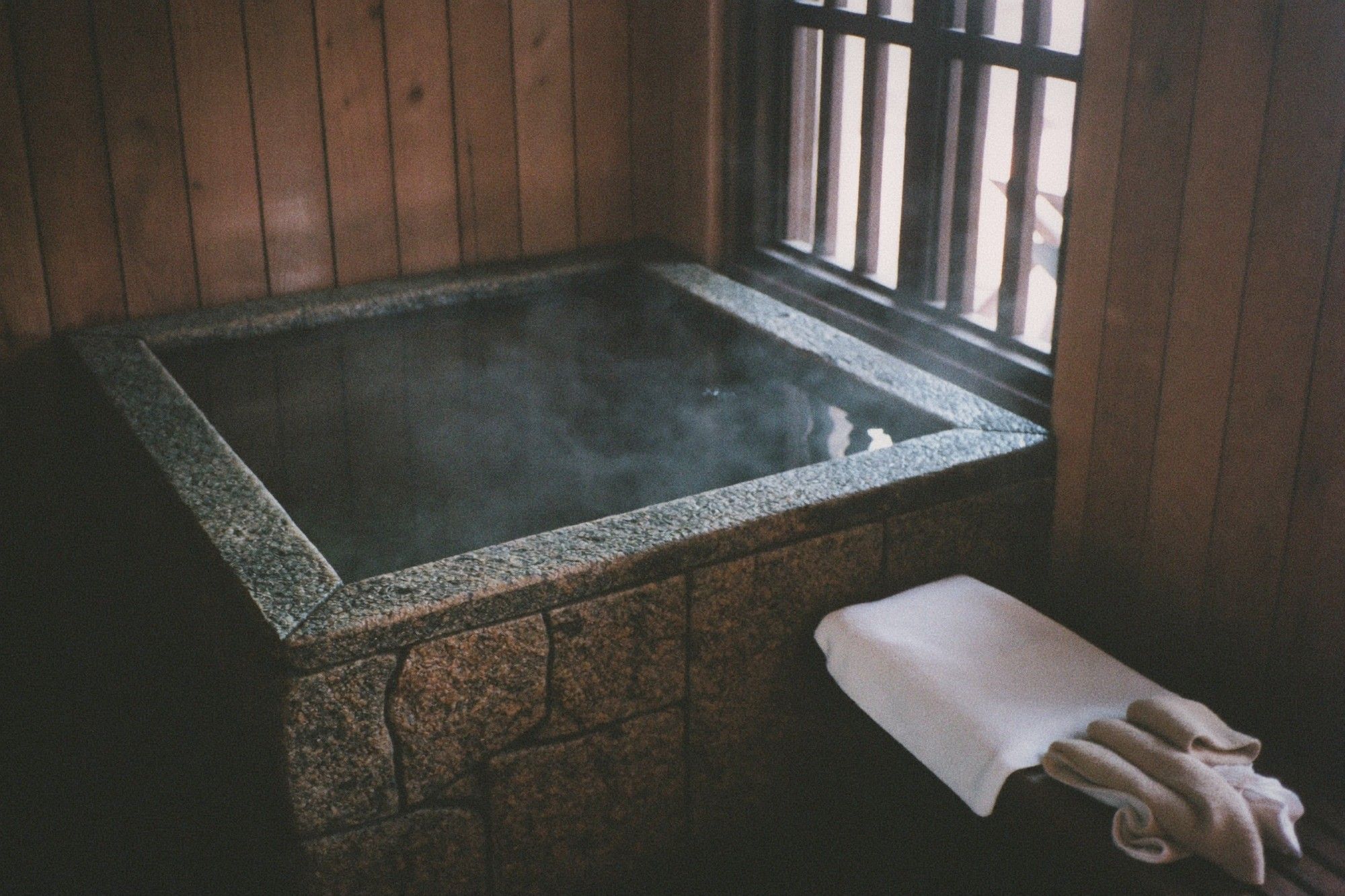 Private indoor hot spring bath with steam rising from a stone tub by a window