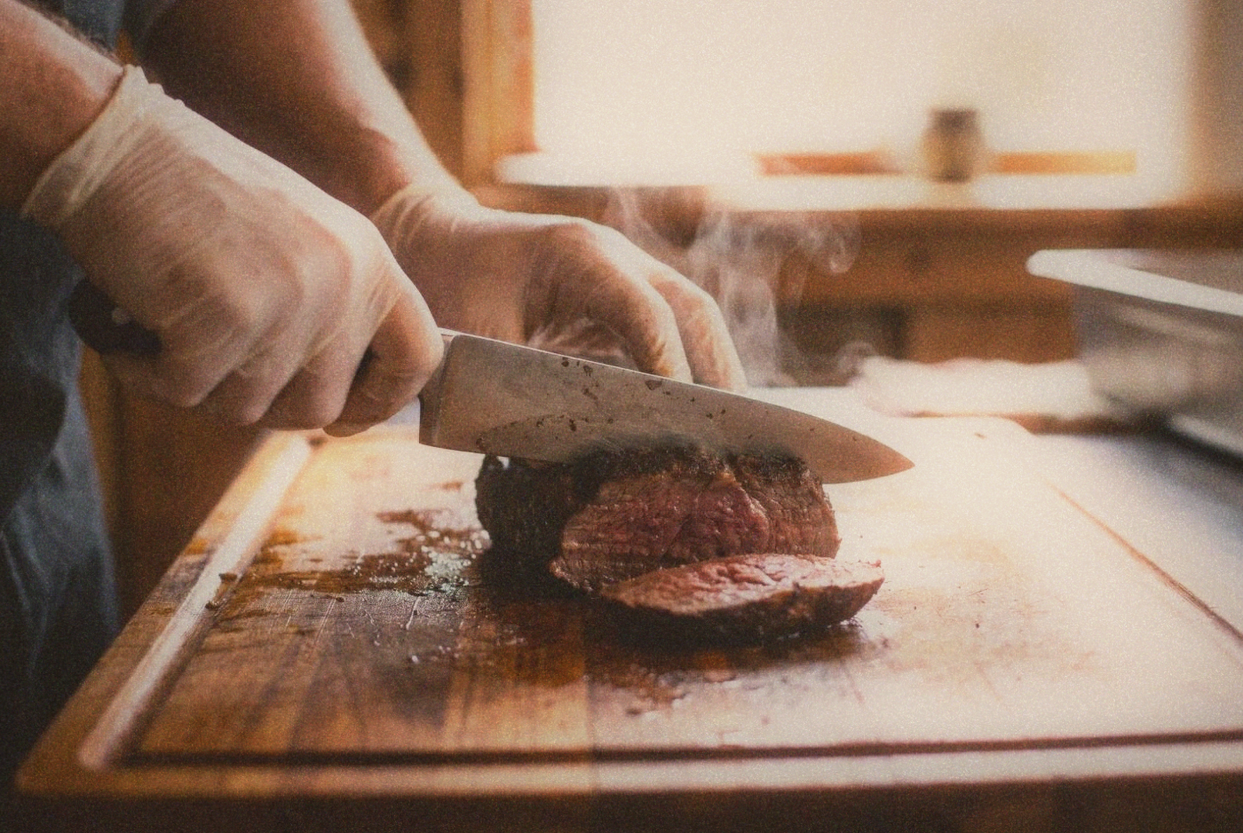 Close-up of butcher hands slicing fresh warm beef on a worn wooden cutting board