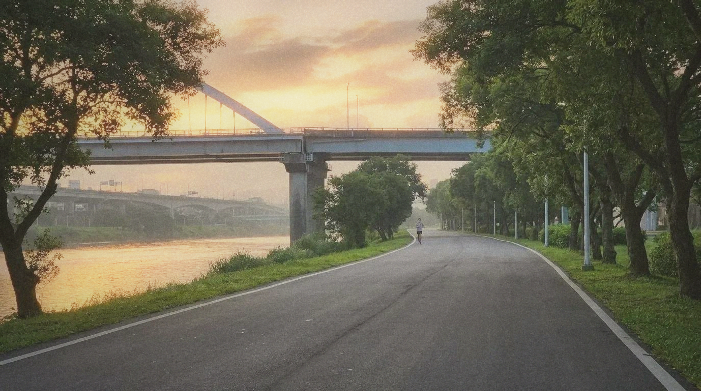 A runner on a wide riverside path in early morning light, Taipei bridges in the background