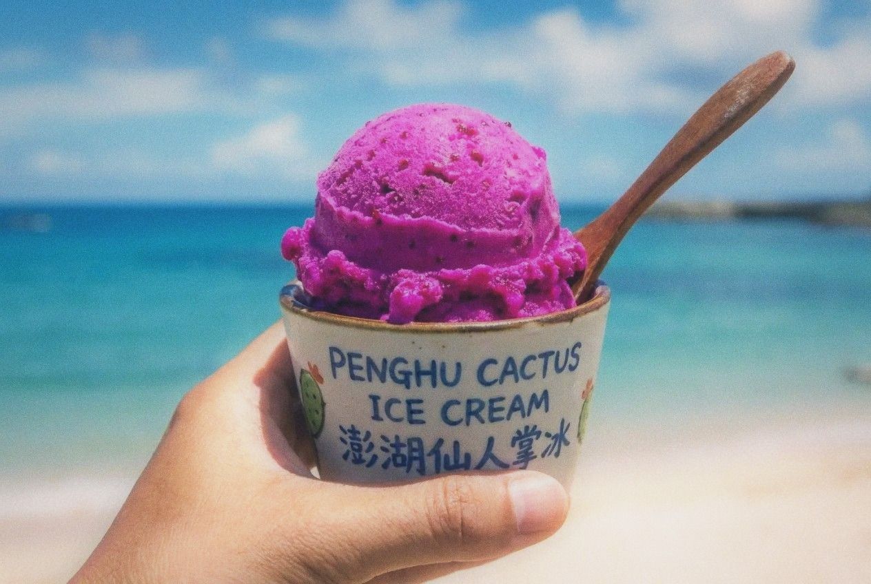 Bright pink-purple scoop of prickly pear cactus ice cream held against ocean background