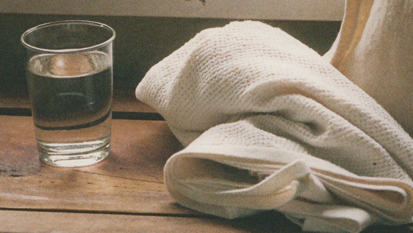 Analogue generated illustration of a water glass and textured cotton towel on a wooden bench.