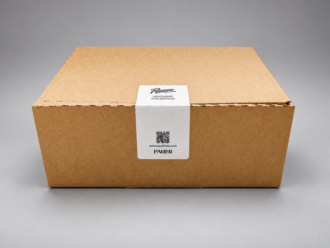 PAUER HATS shipping box sealed with a white sticker: Headwear for Motion, a QR code and pauerhats.com