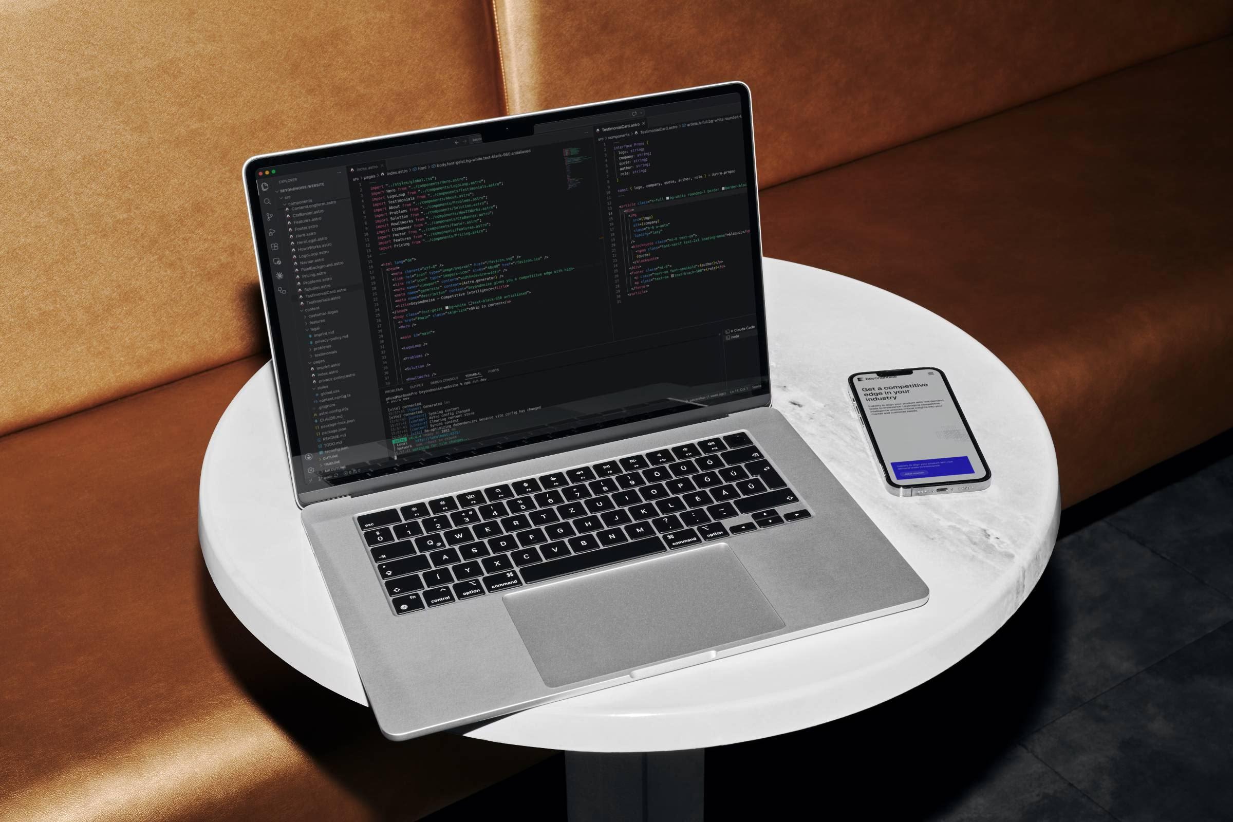 Laptop mit Code-Editor und ein Smartphone auf einem runden Tisch