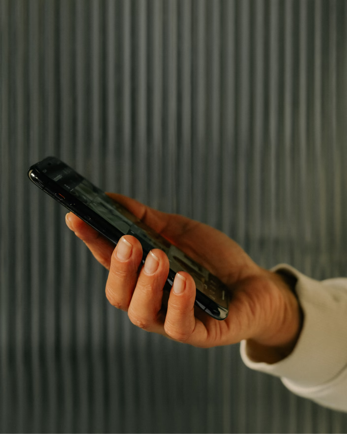 Hand hält ein Smartphone vor einer gerippten Glaswand