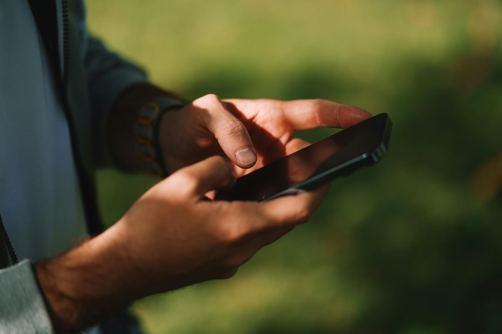 Hände tippen auf einem Smartphone vor grünem Hintergrund