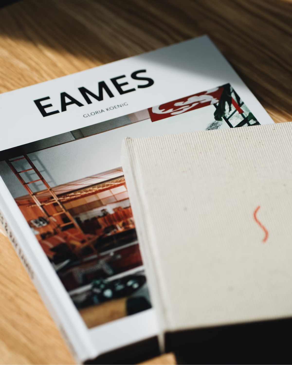 Buch «Eames» und ein Notizbuch auf einem Holztisch