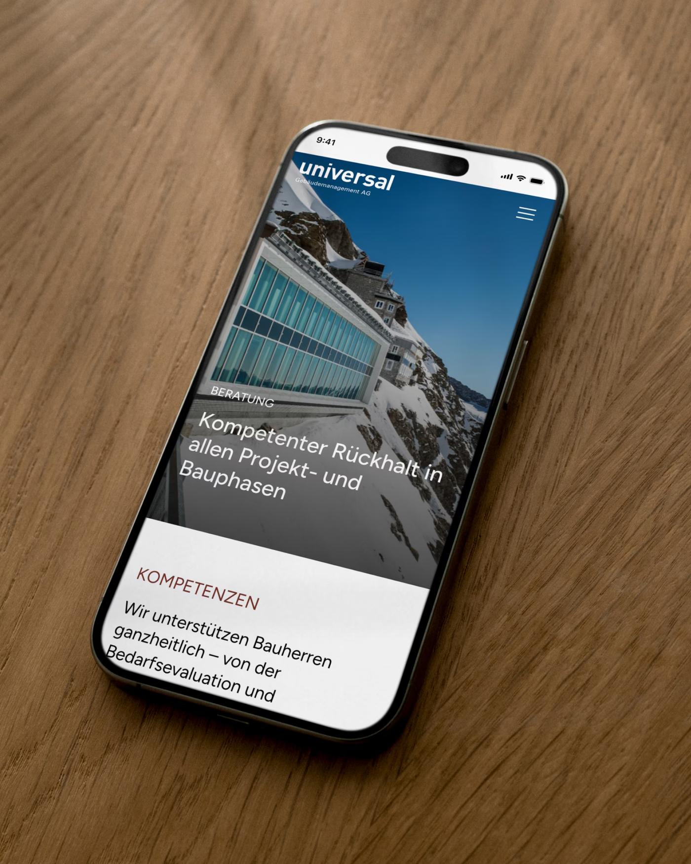 Smartphone mit der Webseite von Universal Gebäudemanagement auf einem Holztisch
