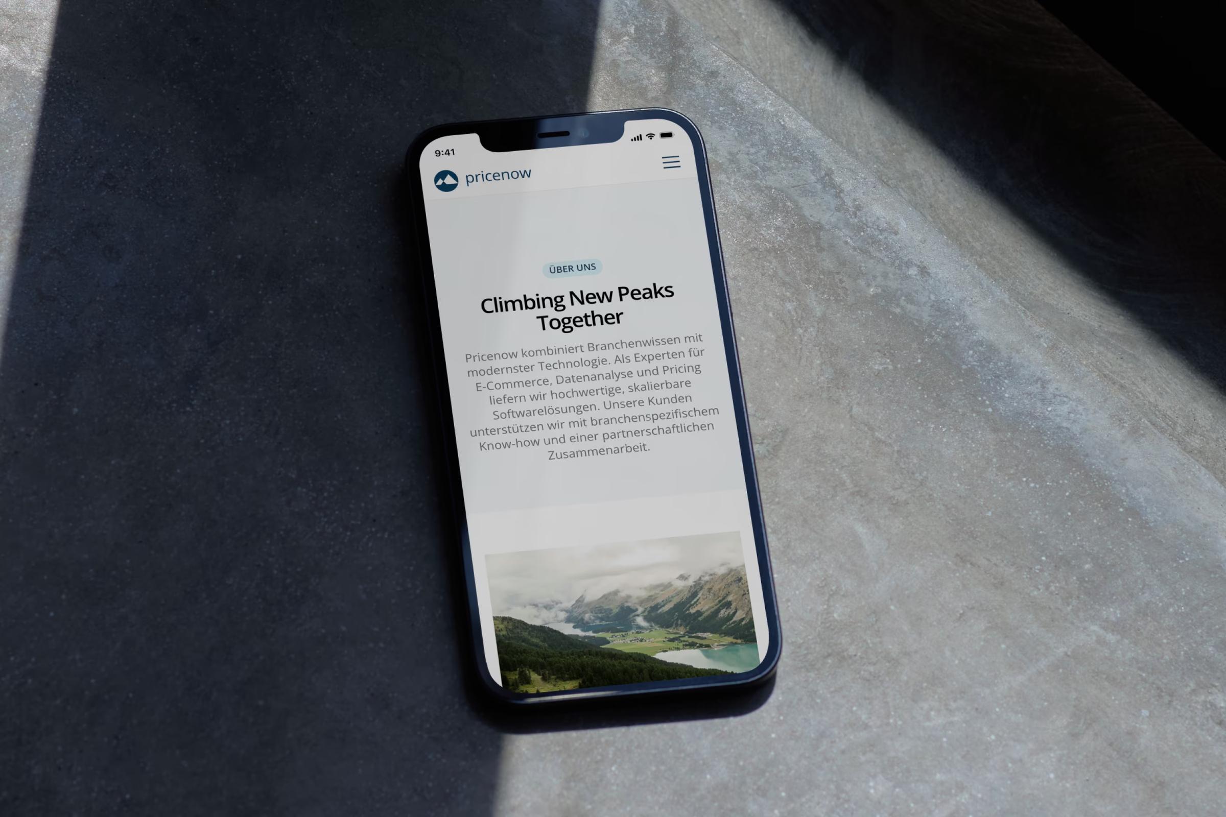 Smartphone mit der Seite «Climbing New Peaks Together» von Pricenow auf Beton
