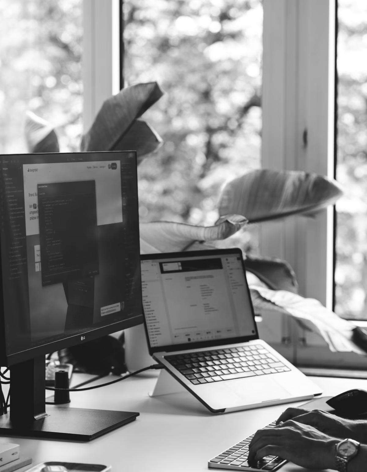 Arbeitsplatz mit Monitor und Laptop, Hände auf der Tastatur, in Schwarzweiss