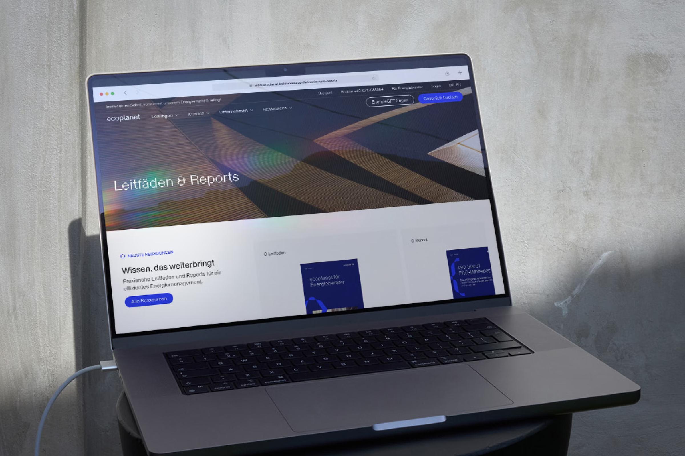 Laptop mit der Seite «Leitfäden & Reports» von ecoplanet vor einer Betonwand