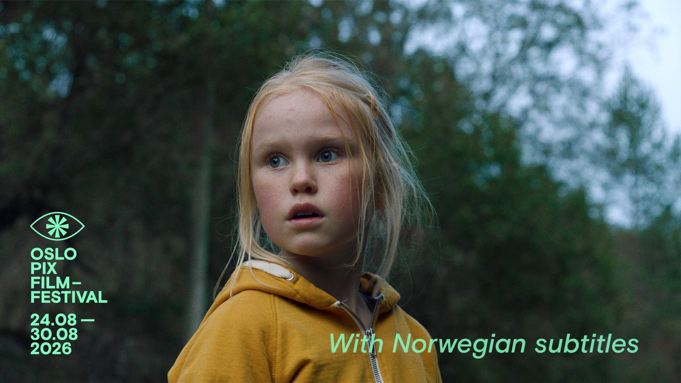 En jente med lyst hår og gul hettegenser står ute foran grønne trær.