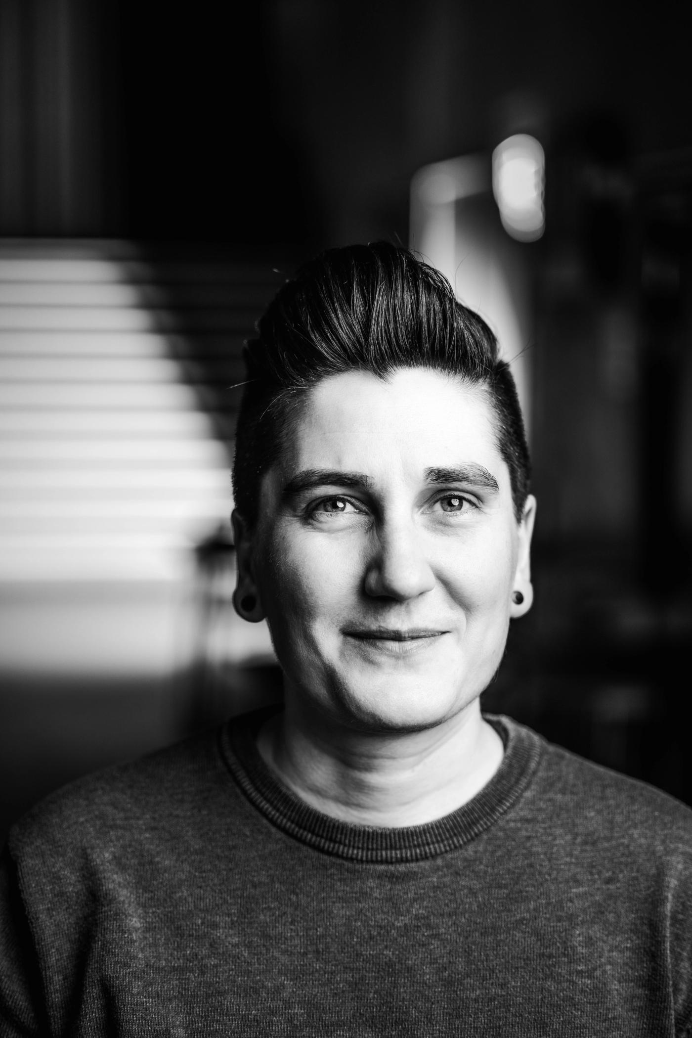 Mørkt kort hår trukket litt bakover og grå genser. Snille øyne og et godt smil.