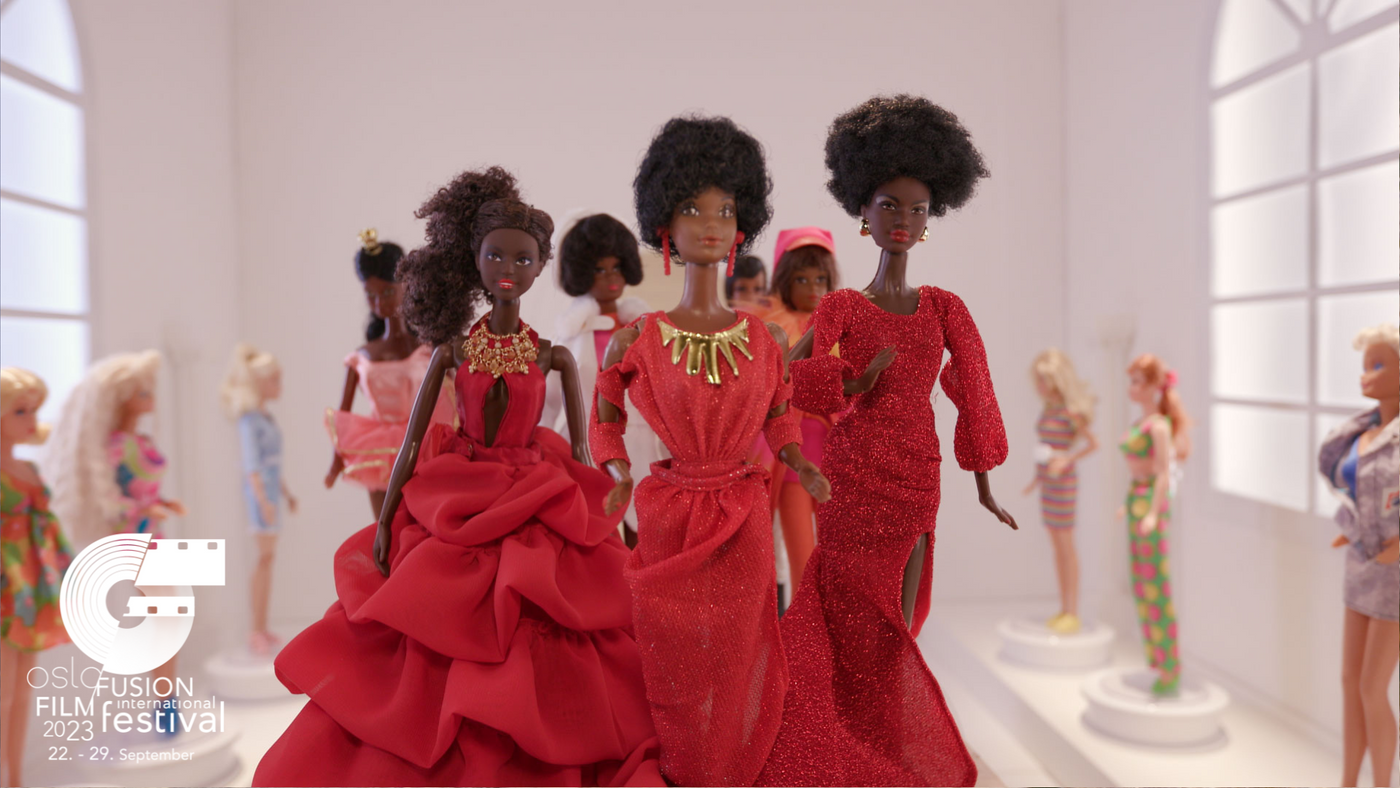 Tre barbie dukker ikledd røde penkjoler står samlet med andre barbie dukker i bakgrunn.