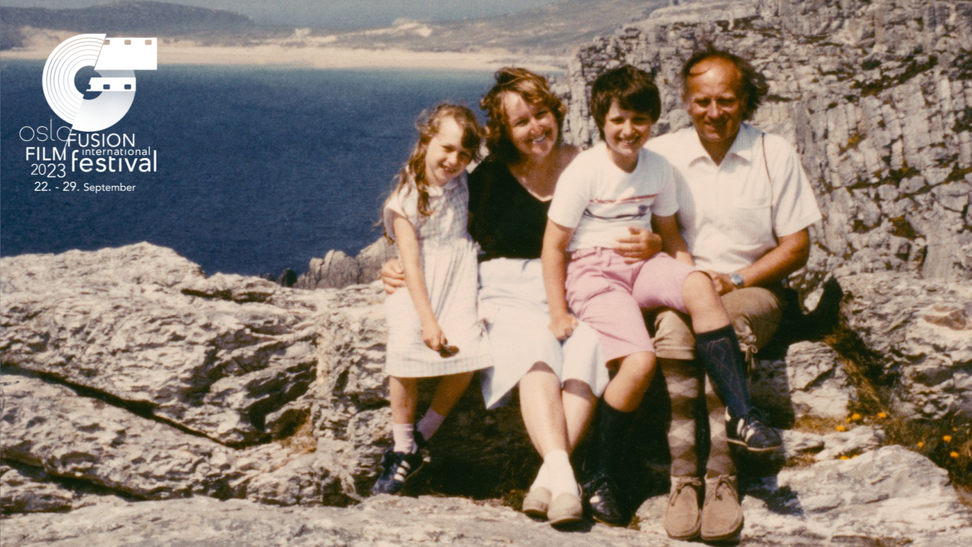 To voksne og to barn sitter sammen på berg foran havet.