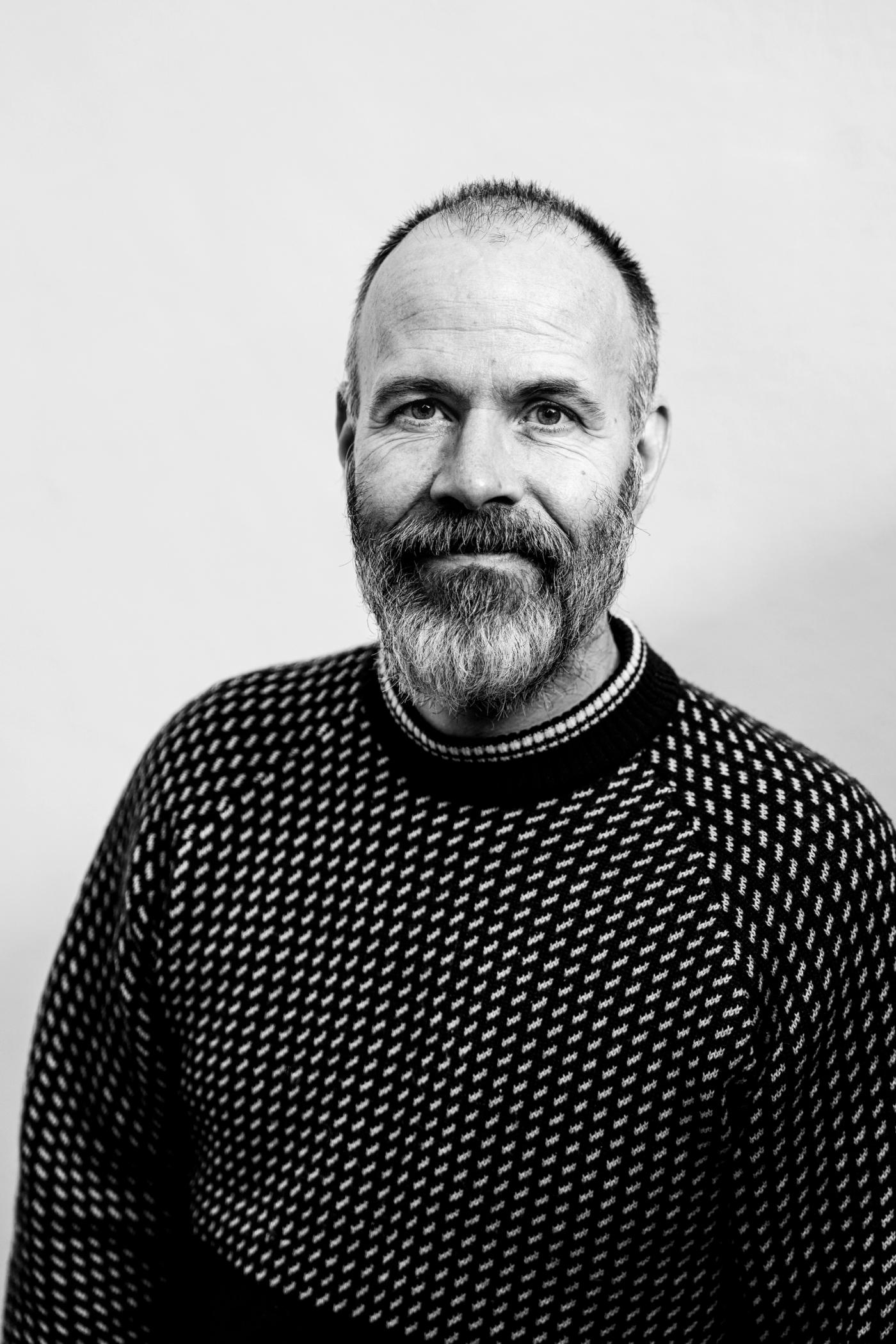 Bilde av skuespiller Espen Løvås i sort/hvitt. Han smiler, har skjegg og sort ullgenser med hvite detaljer.