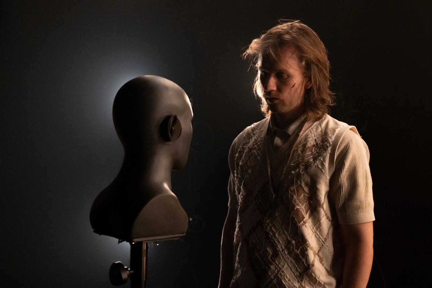 Fredrik i hvor t-skjorte og vest snakker til et hode. 