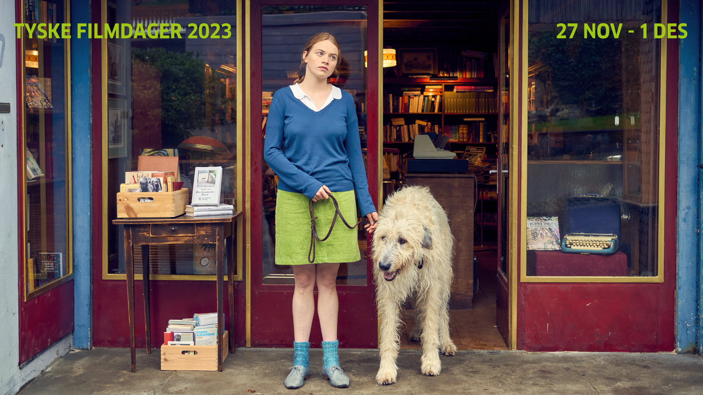 En kvinne med en veldig stor hund står i døråpningen av en butikk